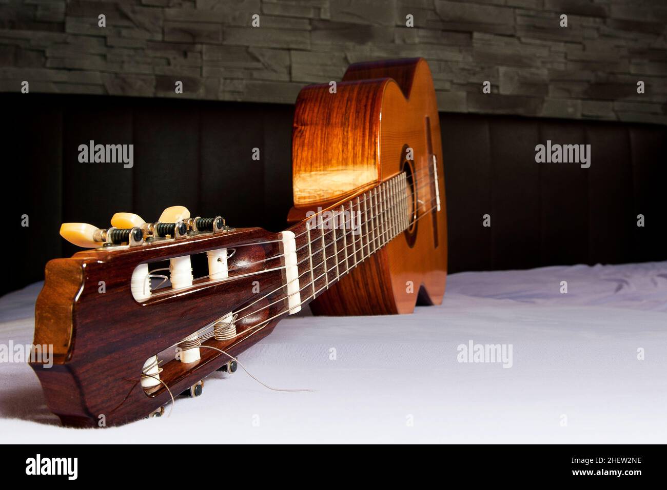 guitare classique couchée sur le lit devant un dos en cuir marron et un mur en pierre Banque D'Images