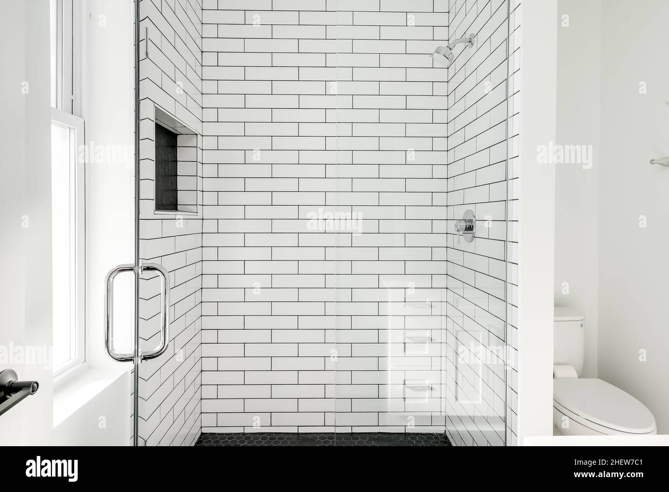 Coffret de douche moderne à carreaux de métro blanc avec plancher en carreaux hexagonaux noirs et porte en verre Banque D'Images