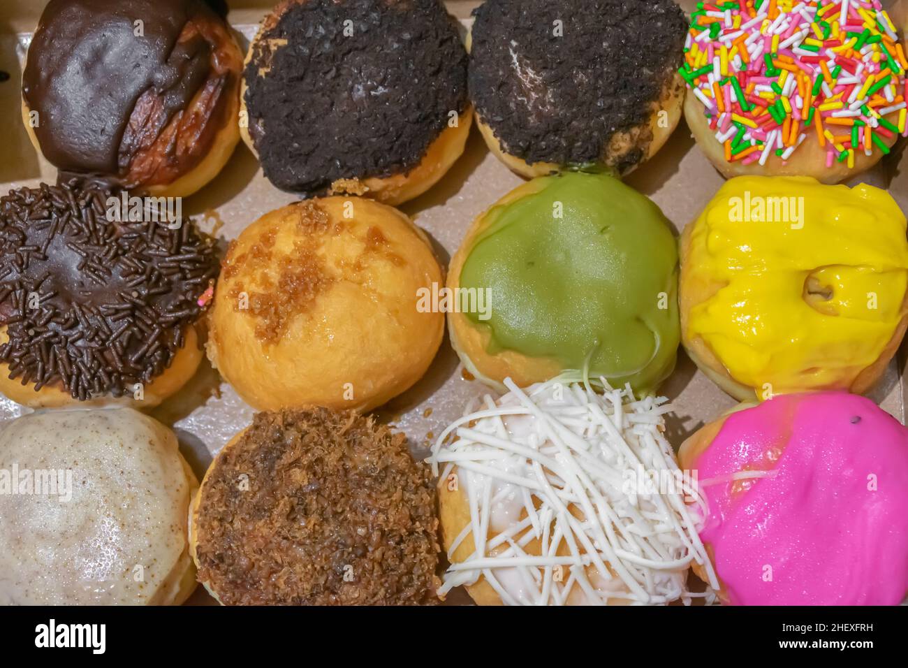 Rangée de beignets délicieux et savoureux avec un assortiment de garnitures colorées à l'envers sur la boîte de papier brun Banque D'Images