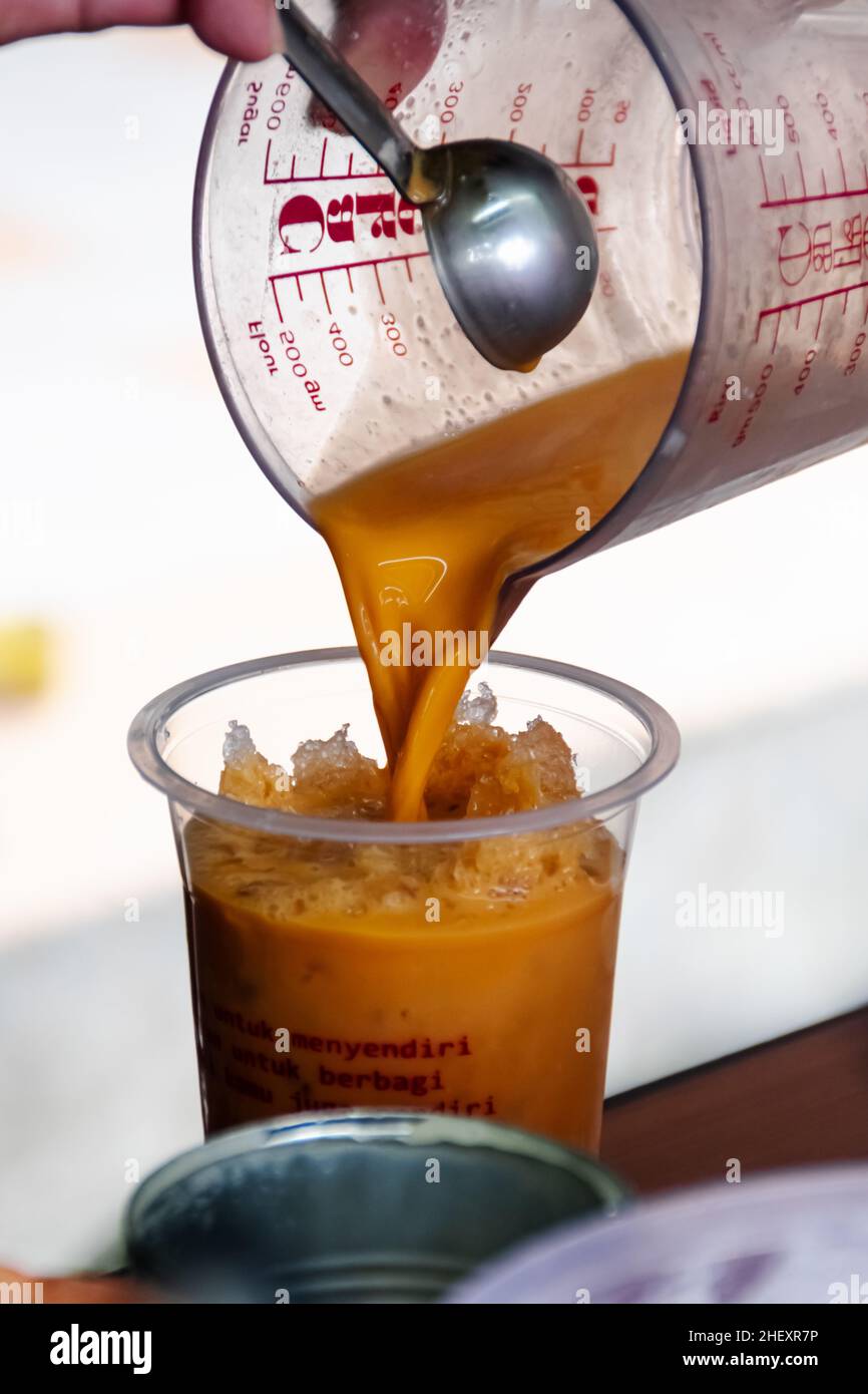 versez un thé thaïlandais au lait frais dans un verre en plastique transparent avec de la glace rasée froide à l'intérieur et du fond flou et doux Banque D'Images