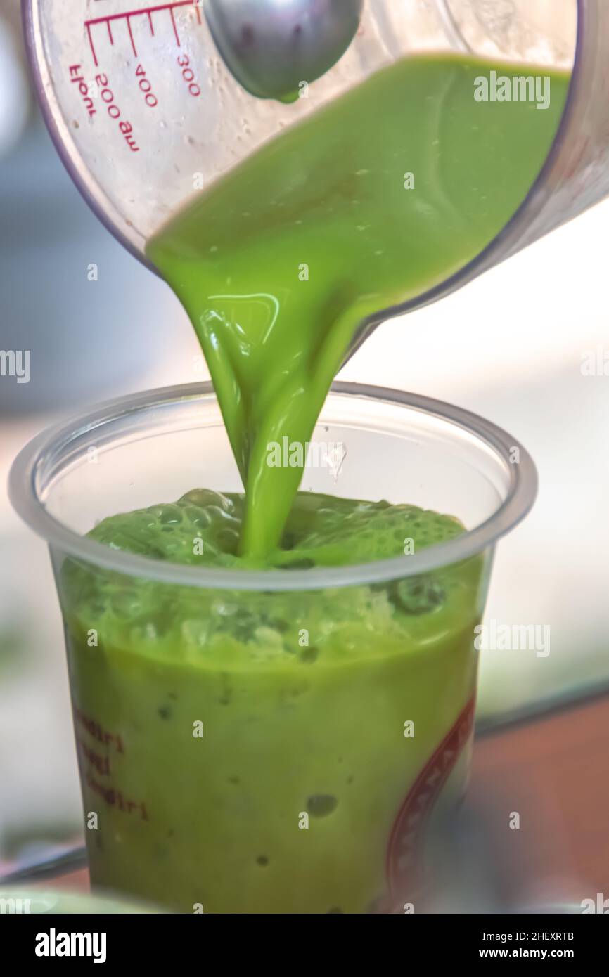 versez un thé vert de lait frais et crémeux dans une tasse graduée dans un verre en plastique transparent avec de la glace rasée froide à l'intérieur avec un bac flou et doux Banque D'Images