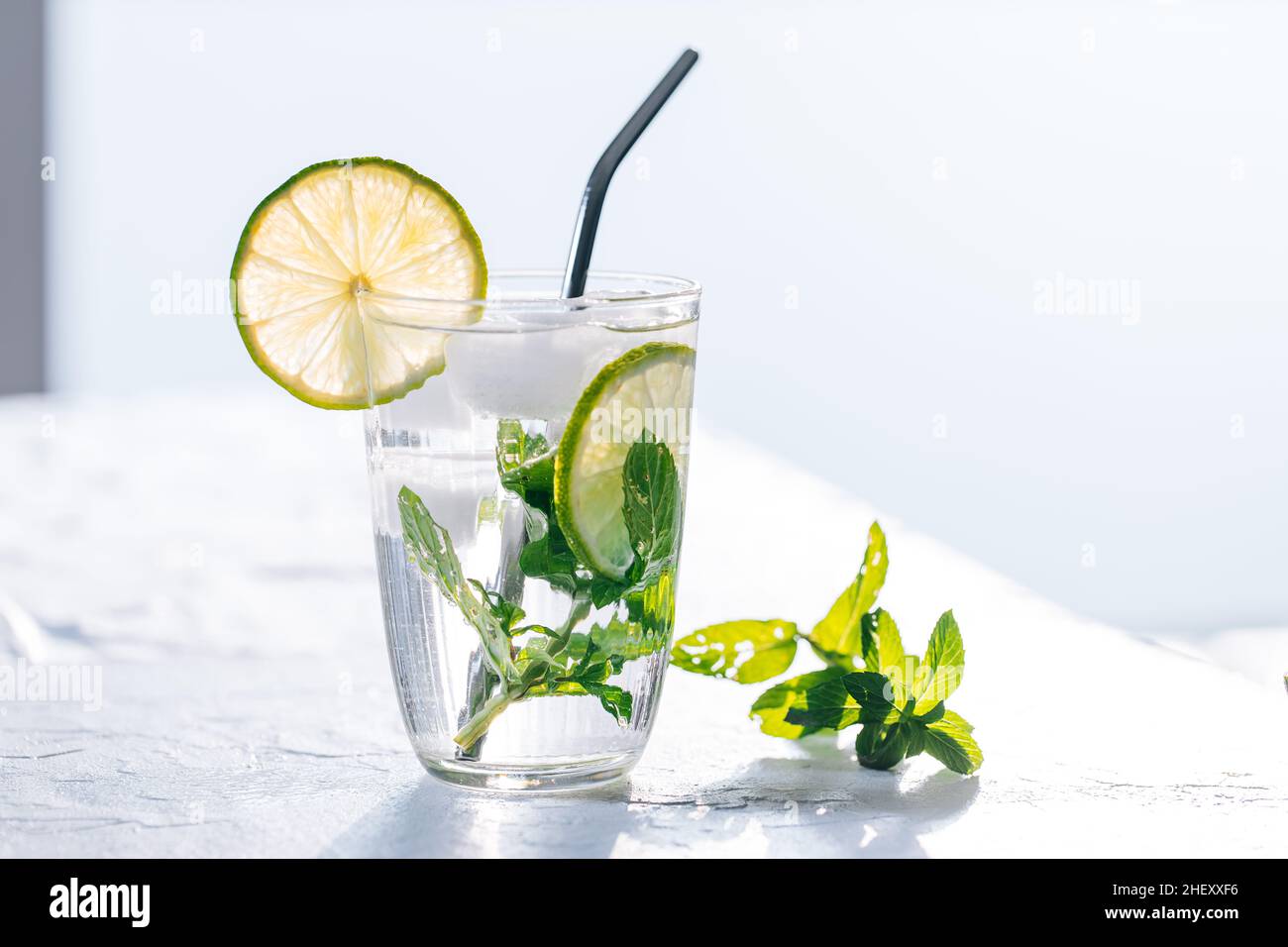 Mojito cocktail en verre avec citron vert, glace et menthe servi sur un fond lumineux Banque D'Images