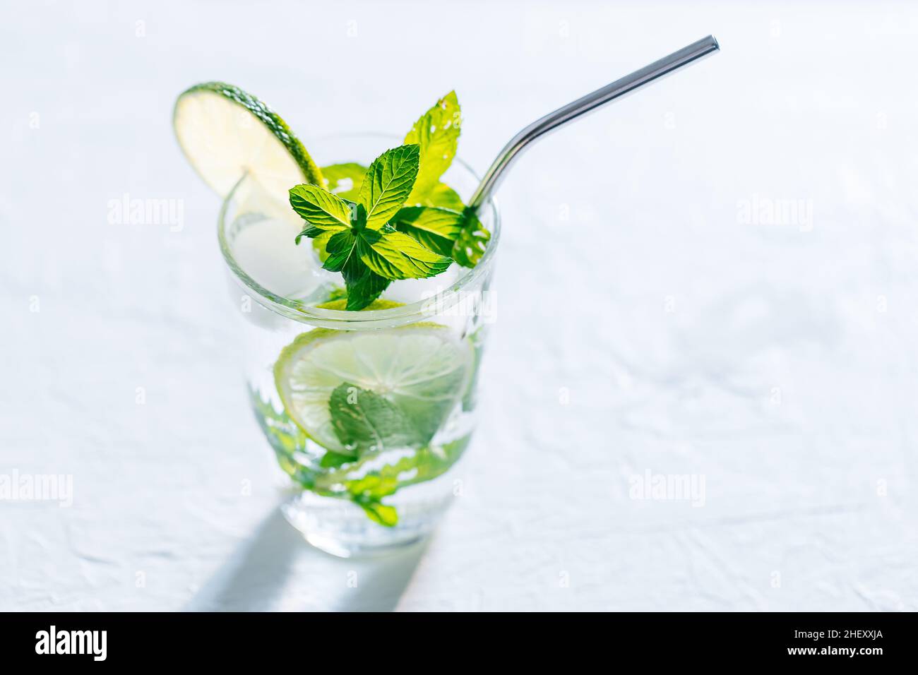 Mojito cocktail en verre avec citron vert, glace et menthe servi sur un fond lumineux Banque D'Images