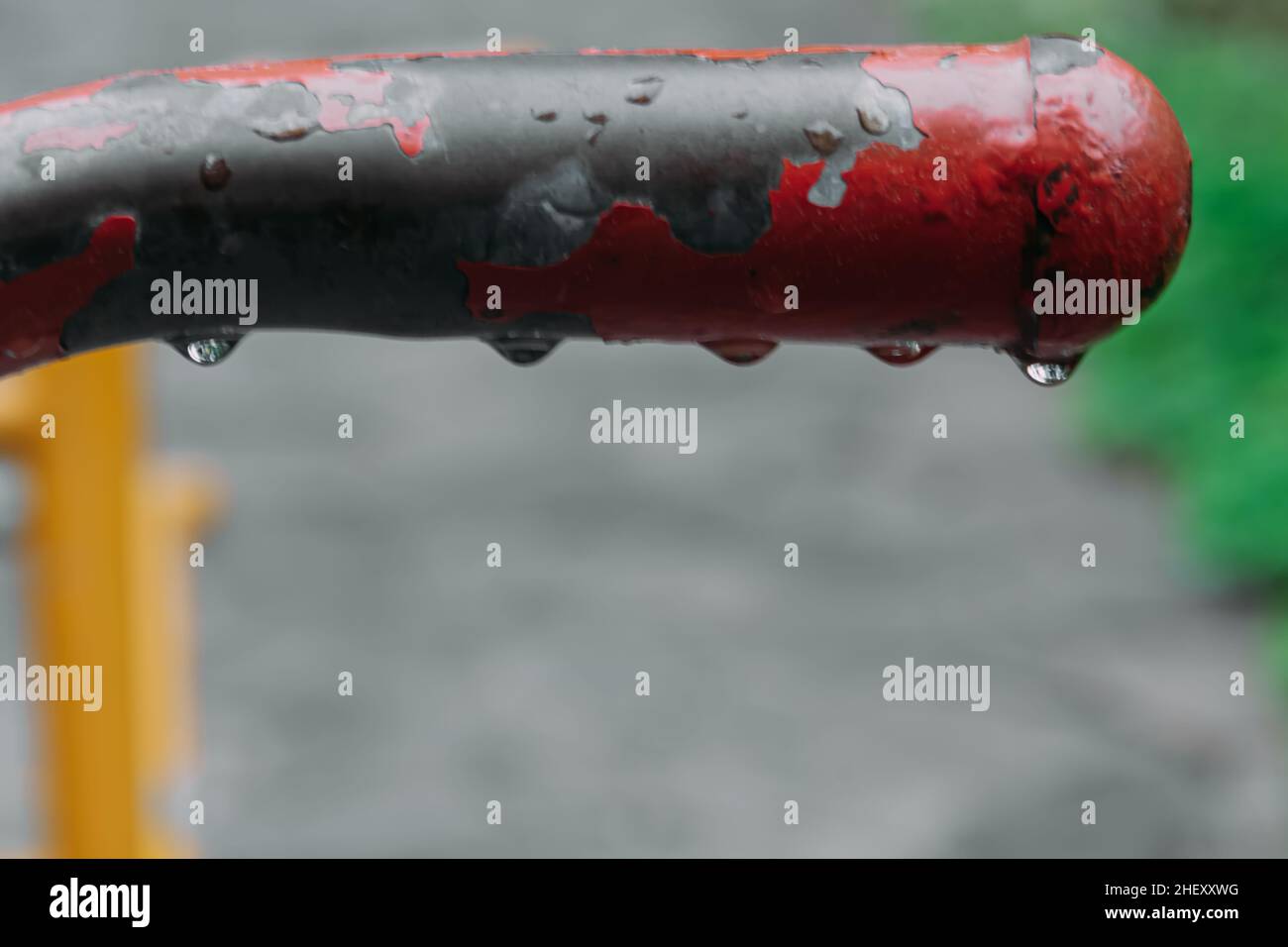 Un tas de gouttes d'eau s'accumulent sous le tuyau en acier rustique rouge rugueux du parc de la ville avec un arrière-plan flou et flou Banque D'Images