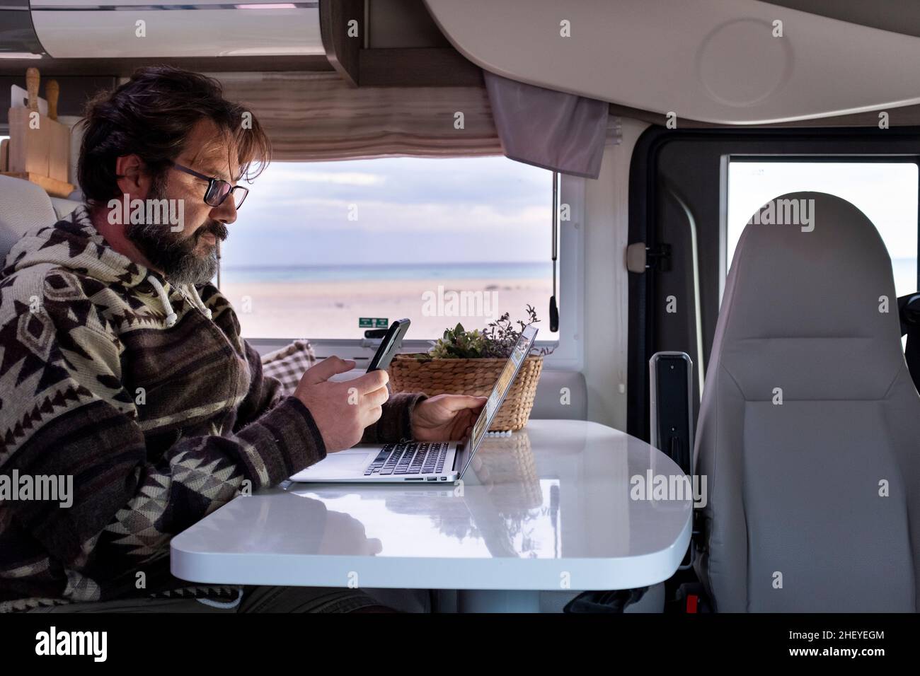 Homme adulte travaillant avec un ordinateur portable à l'intérieur d'une camionnette de camping.Liberté de vie des travailleurs à distance.Utilisation intelligente du téléphone et connexion en itinérance.Voiture de camping inter Banque D'Images