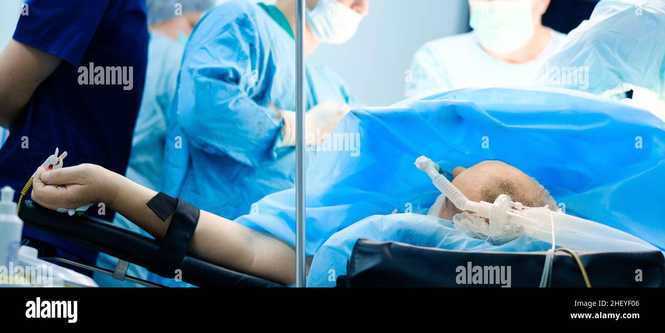 Une personne inconnue se trouve sur la table d'opération pendant la chirurgie.Mise au point sélective.Le patient est inconscient et connecté au système de ventilation pulmonaire artificielle.Arrière-plan flou.Image grand écran. Banque D'Images