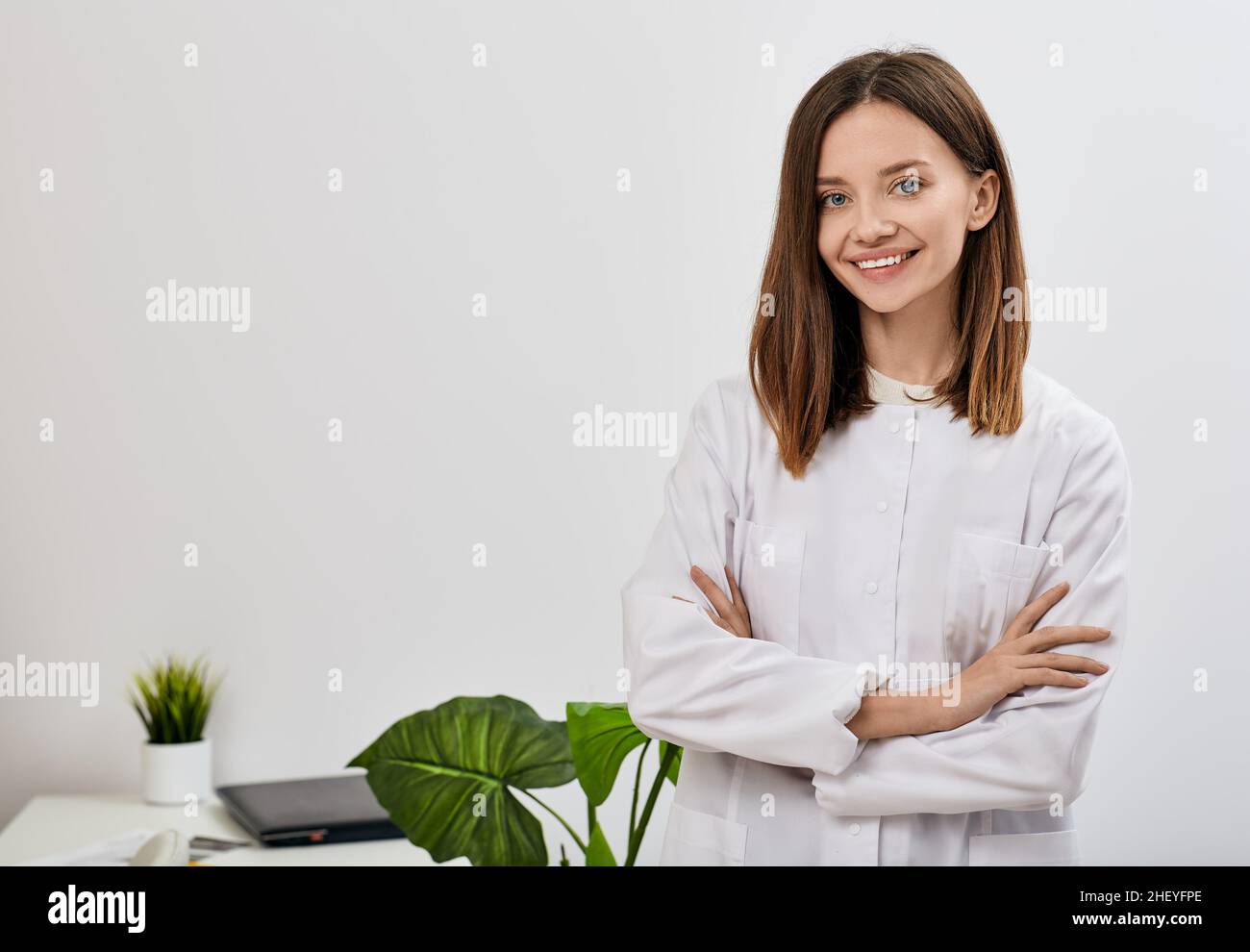 Médecin femme souriante avec les bras croisés debout devant son cabinet de médecin et regardant la caméra. concept d'occupation médicale avec espace pour le texte Banque D'Images