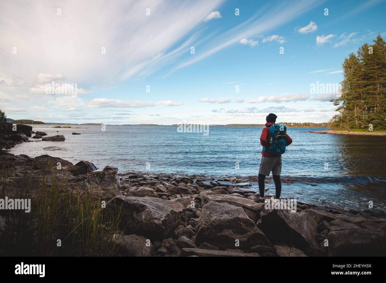 Le randonneur portant une veste et portant un sac à dos marche le long de la plage et regarde le lac Jatkonjarvi au coucher du soleil dans le parc national de Koli, dans l'est de la Finlande.Ma Banque D'Images