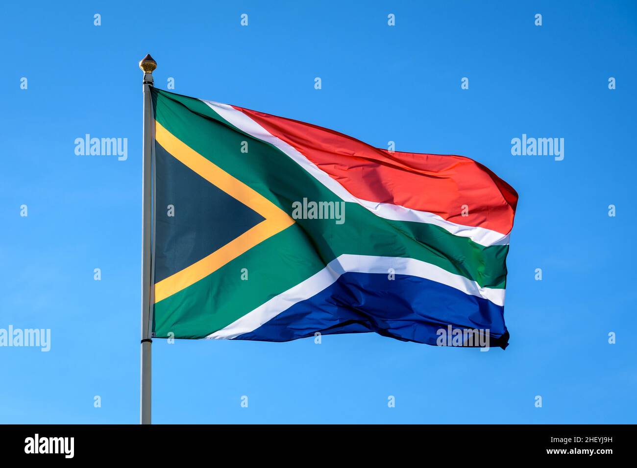 Le drapeau national de l'Afrique du Sud vole dans le vent en mât complet contre le ciel bleu. Banque D'Images