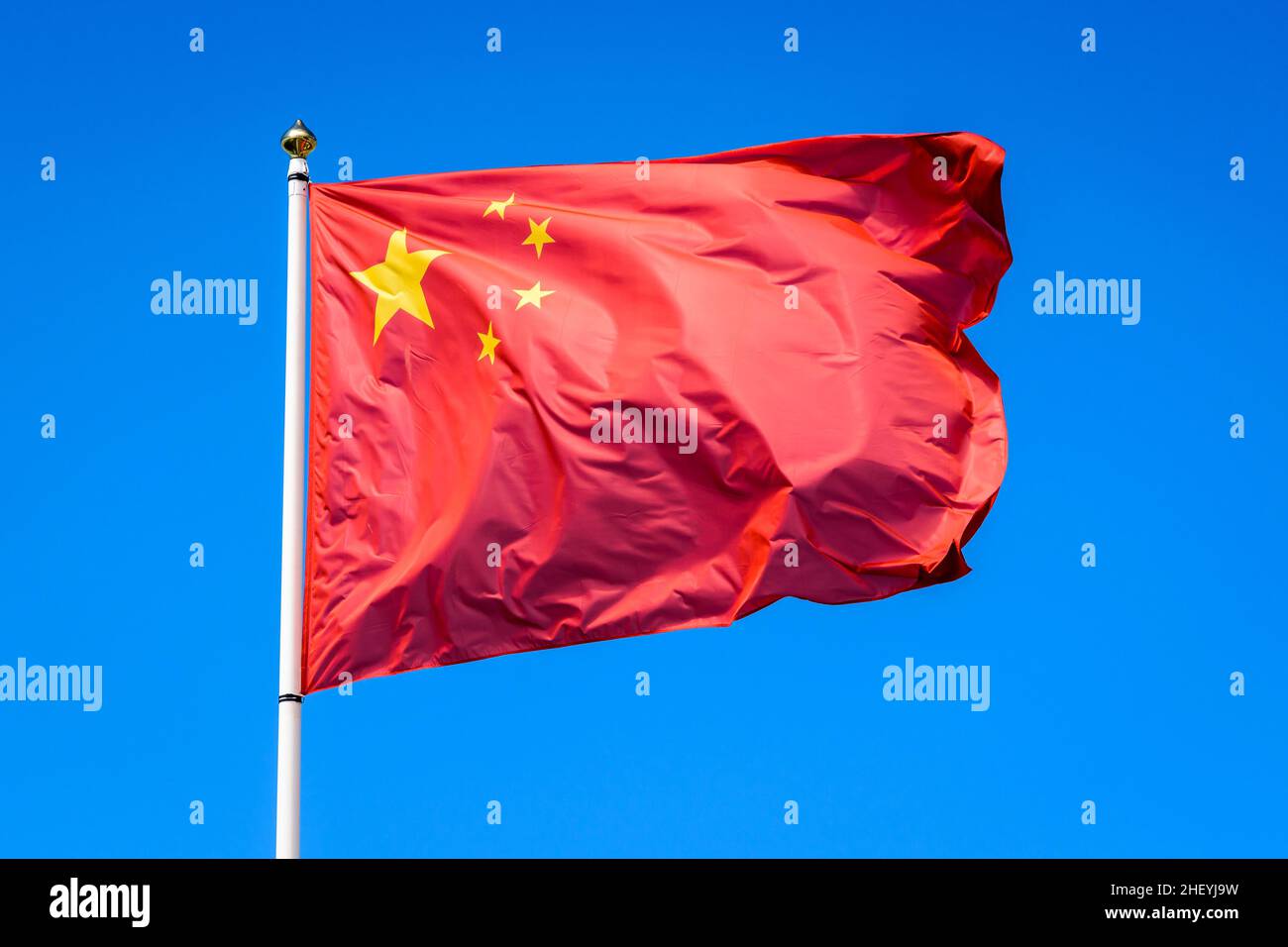 Le drapeau national de la République populaire de Chine vole dans le vent en mât complet contre le ciel bleu. Banque D'Images