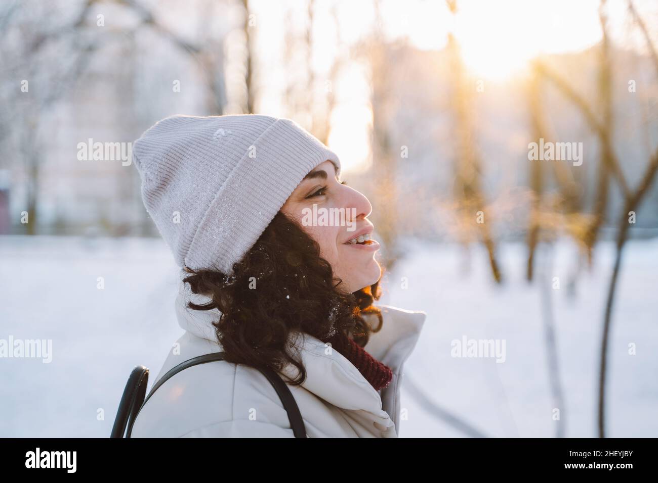 Une jeune femme brunette aux cheveux bouclés marche en hiver dans la rue respire de l'air givré avec de la vapeur de sa bouche.Vue latérale. Banque D'Images