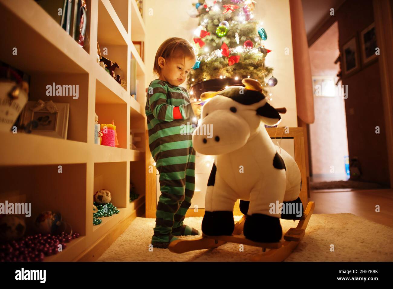 Bebe Fille Sur Le Jouet De Vache A Bascule Contre L Arbre De Noel Avec Des Guirlandes Brillantes Le Soir A La Maison Photo Stock Alamy