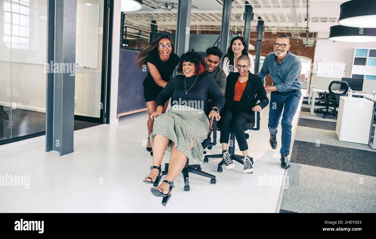 Des hommes d'affaires qui s'amusent au bureau.Un groupe de collègues joyeux  se poussant les uns les autres sur des chaises dans un lieu de travail  moderne.Des hommes d'affaires heureux Photo Stock -