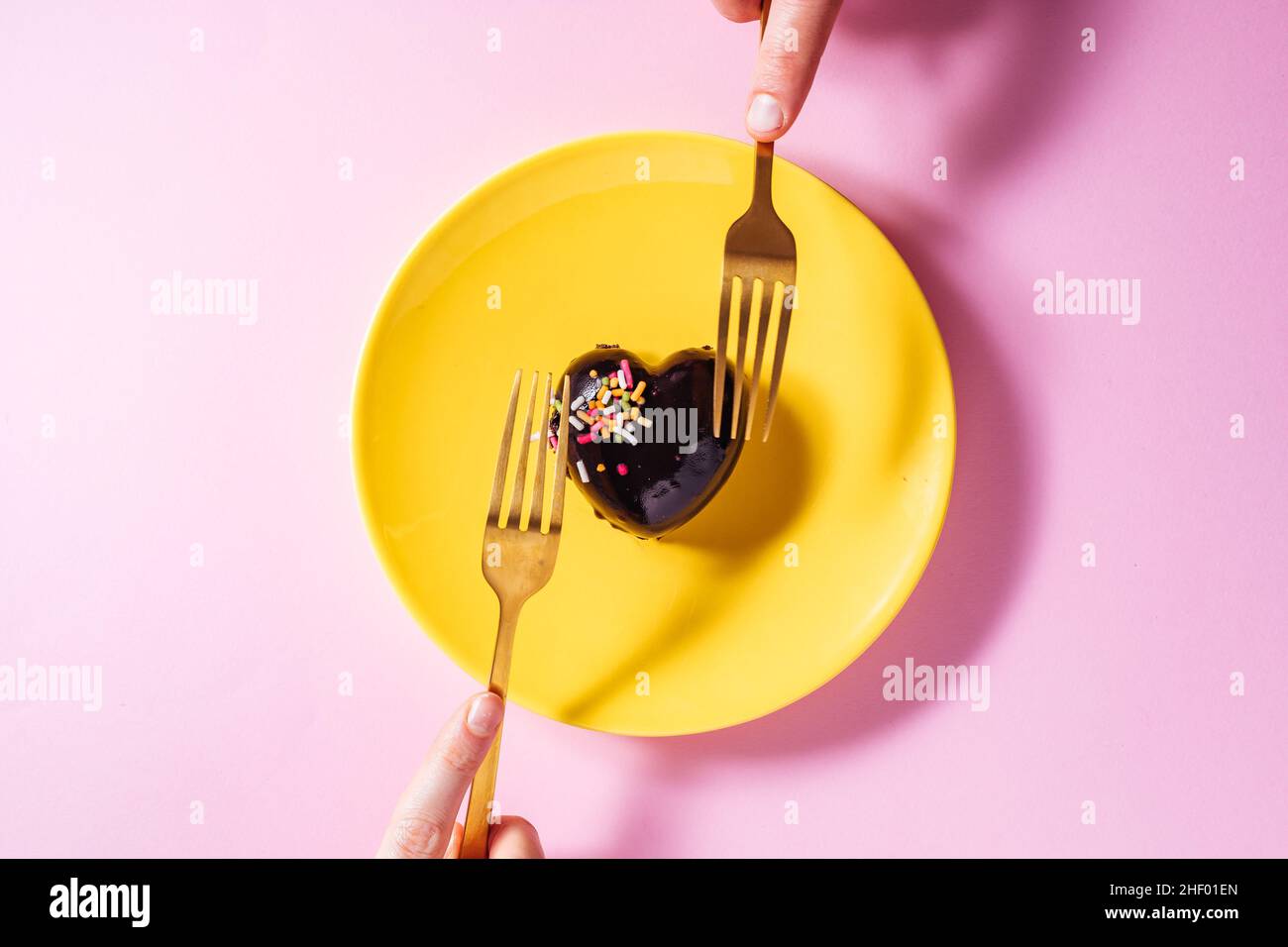 Gâteau au chocolat en forme de coeur sur une assiette jaune avec pralines au chocolat en forme de coeur sur un fond violet avec deux rubans rouges.Saint Valentin Banque D'Images