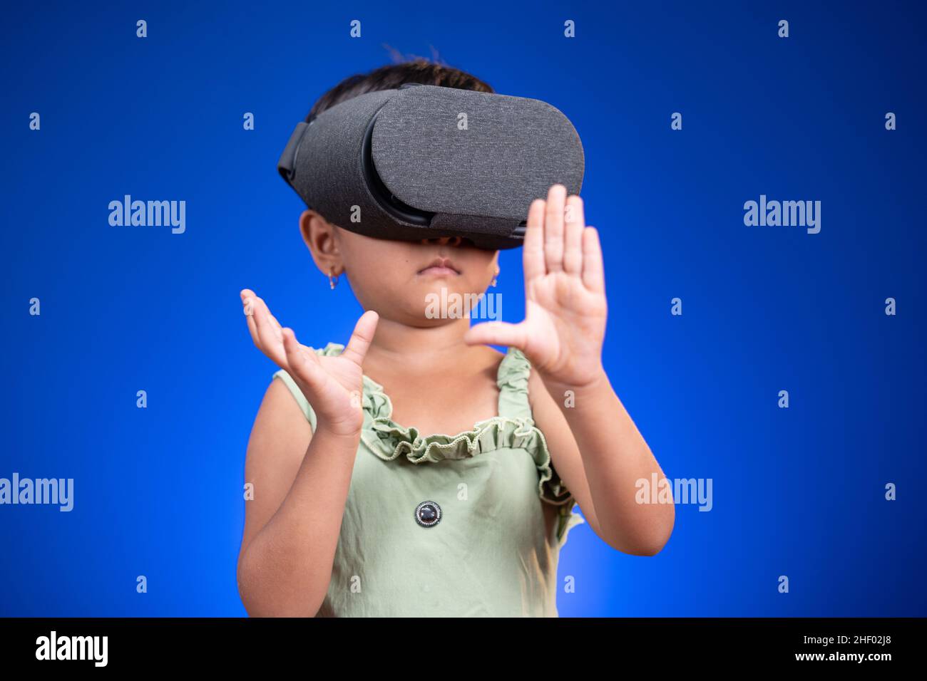 Litle girl gamin appréciant VR ou des lunettes virtuelles en se sentant sur fond bleu - concept d'enfants utilisant la technologie moderne de divertissement et de génération Banque D'Images