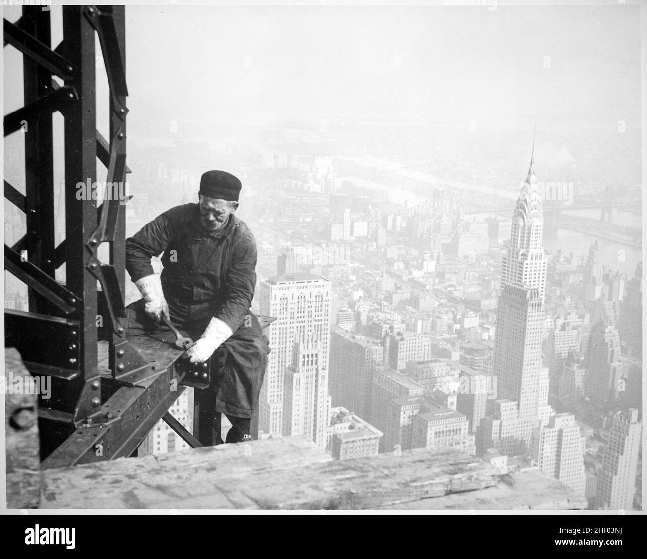 Photographie d'un ouvrier de la construction boulonné des poutres sur le cadre de l'Empire State Building.En arrière-plan (à droite) se trouve le Chrysler Building. Banque D'Images