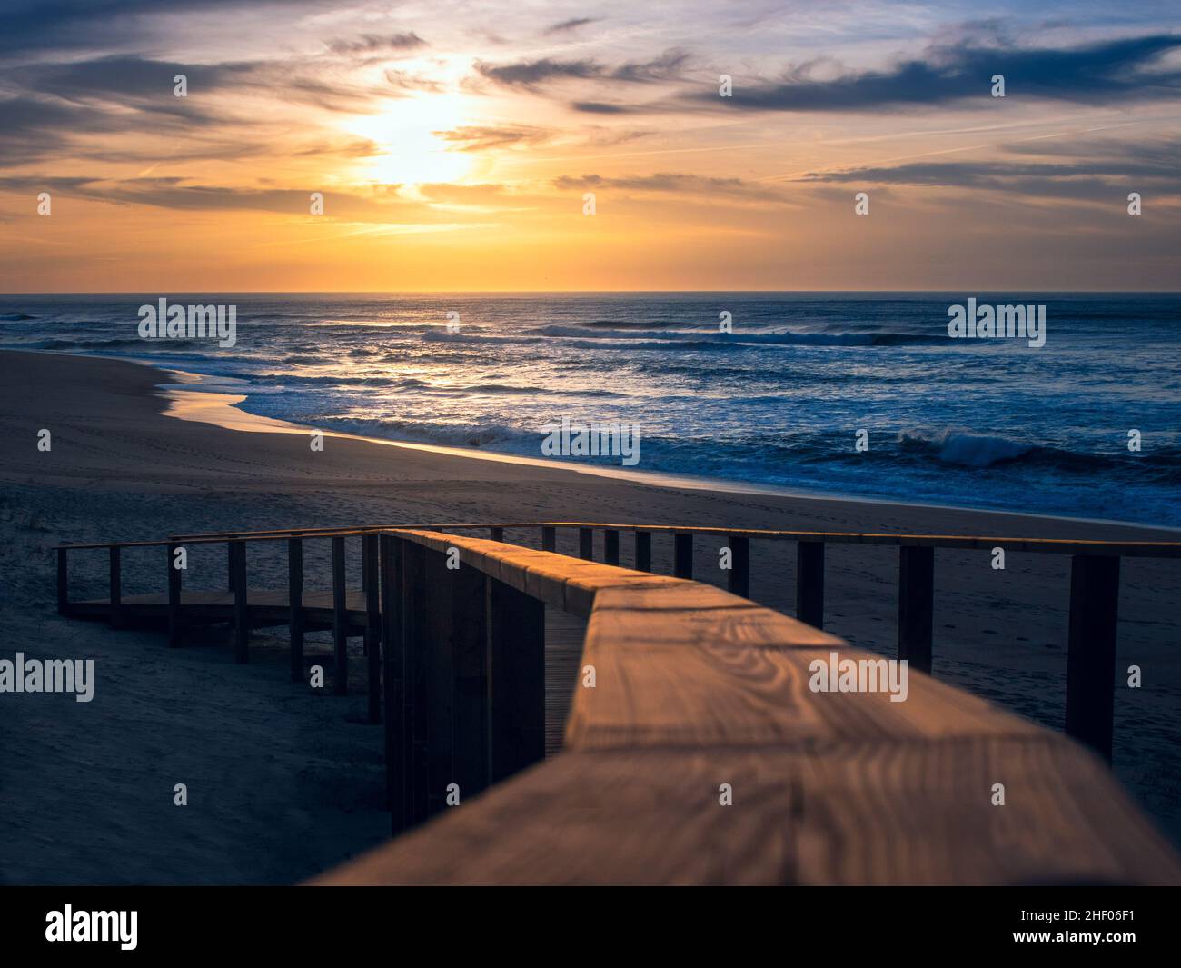 Paysage de coucher de soleil doré sur la plage montrant un gros plan flou de la main courante en bois de la promenade menant au sable et à l'océan Atlantique Banque D'Images