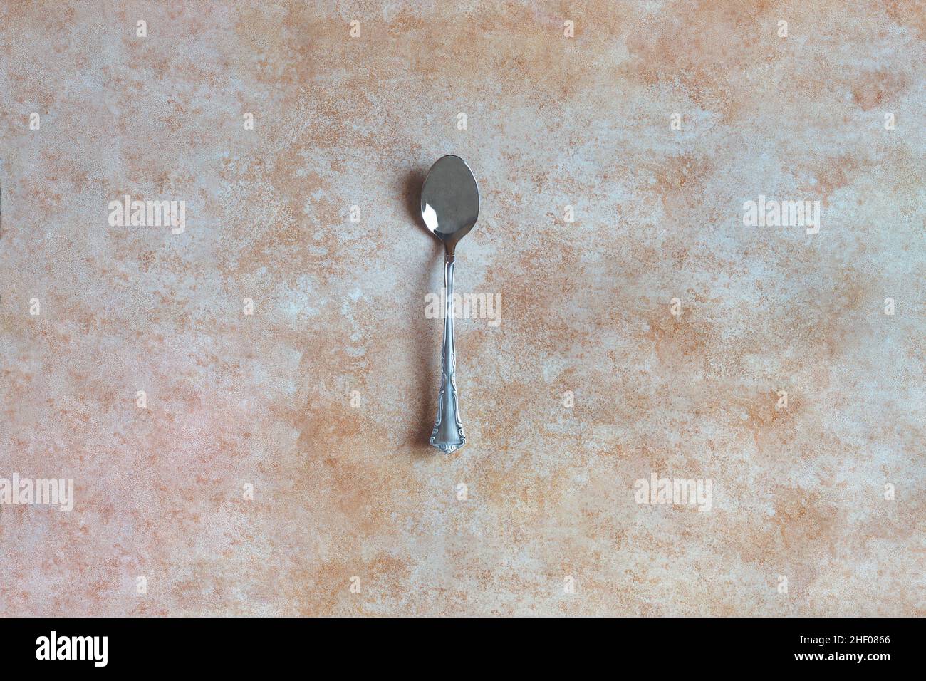 Vue de dessus d'une cuillère en argent antique isolée sur un fond abstrait texturé de couleur pastel.Antiquités et métaux. Banque D'Images
