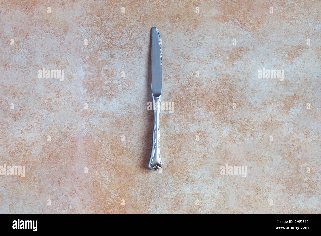 Vue de dessus d'un couteau rond argenté antique sur un arrière-plan et une texture de couleur pastel abstraites.Antiquités et métaux. Banque D'Images