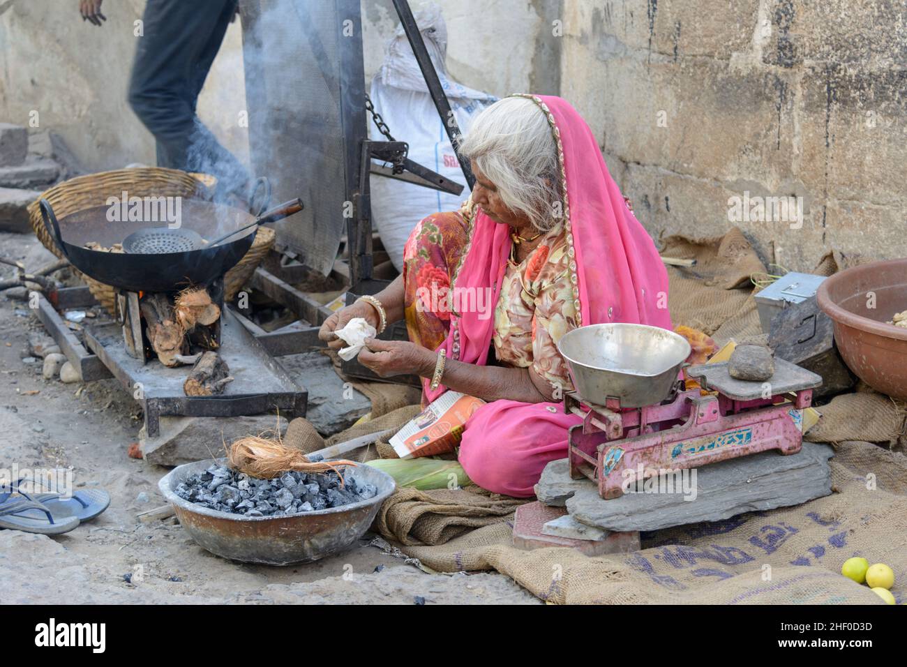 Une femme indienne âgée de la région portant un rose sari cuisine la nourriture de rue sur un feu de charbon de bois dans le village de Nagda, près d'Udaipur, Rajasthan, Inde Banque D'Images