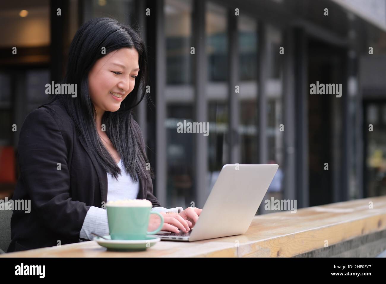 Portrait d'une jeune femme d'affaires asiatique souriante travaillant sur un ordinateur portable dans un café en plein air Banque D'Images