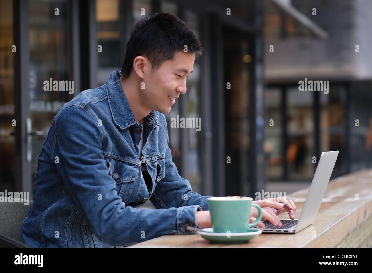 Portrait d'un jeune asiatique assis dans un café en plein air, souriant et dactylographiant sur un ordinateur portable Banque D'Images