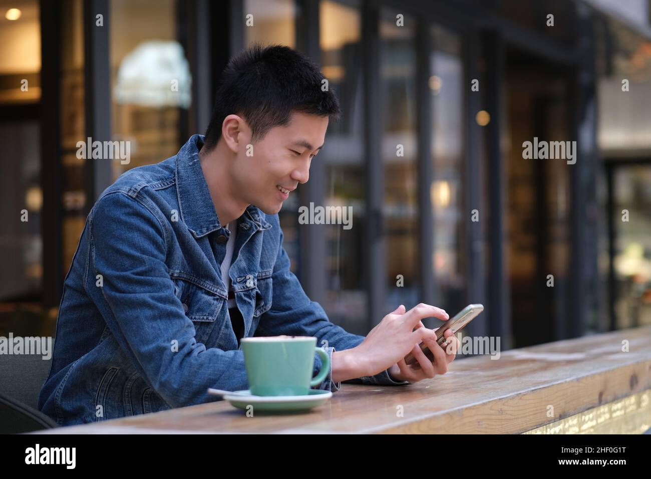 Portrait du jeune homme asiatique au café extérieur, en utilisant le téléphone portable, avec une sourires heureuse Banque D'Images