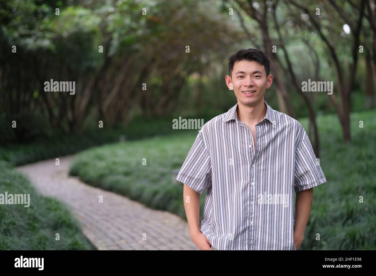 Un jeune homme asiatique souriant et regardant l'appareil photo dans un parc vert naturel Banque D'Images