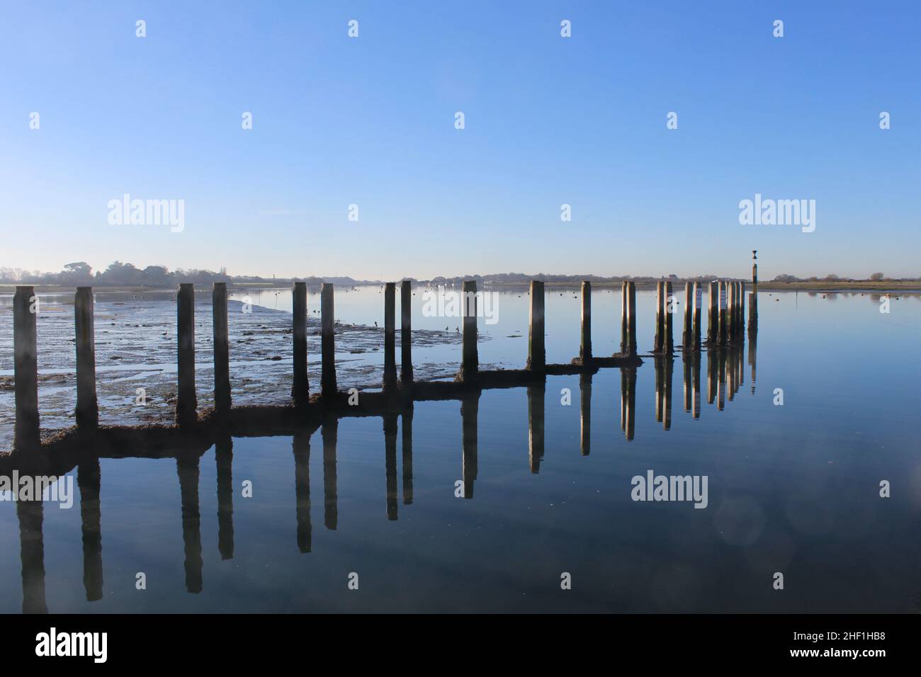 Les postes d'amarrage à Bosham Quay se reflètent dans les eaux fixes.Espace de copie bleu clair pour ajouter du texte. Banque D'Images