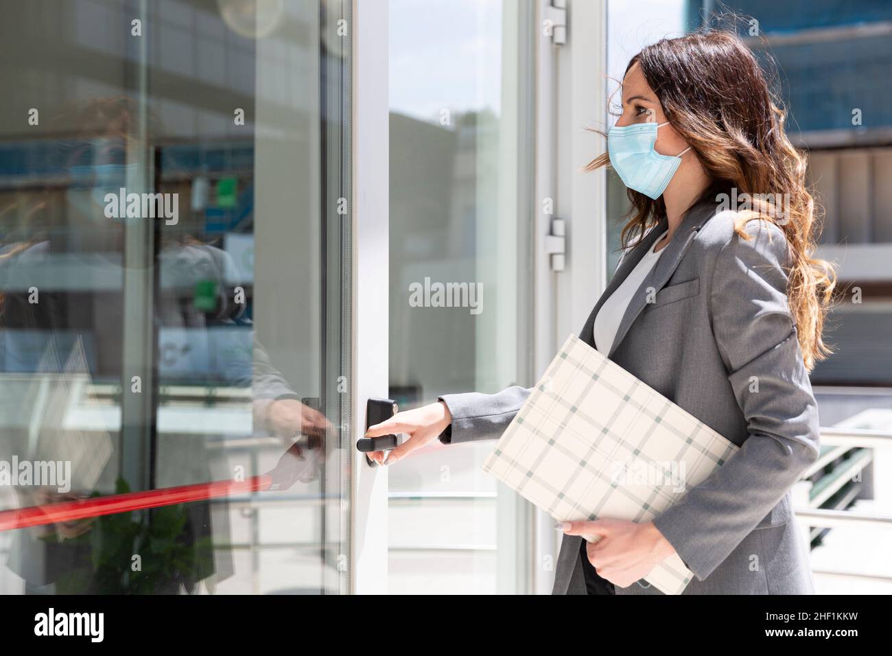 Jeune femme d'affaires blanche élégante qui entre dans son lieu de travail.Elle porte un masque médical pour prévenir la propagation du virus Covid-19.Espace pour tex Banque D'Images