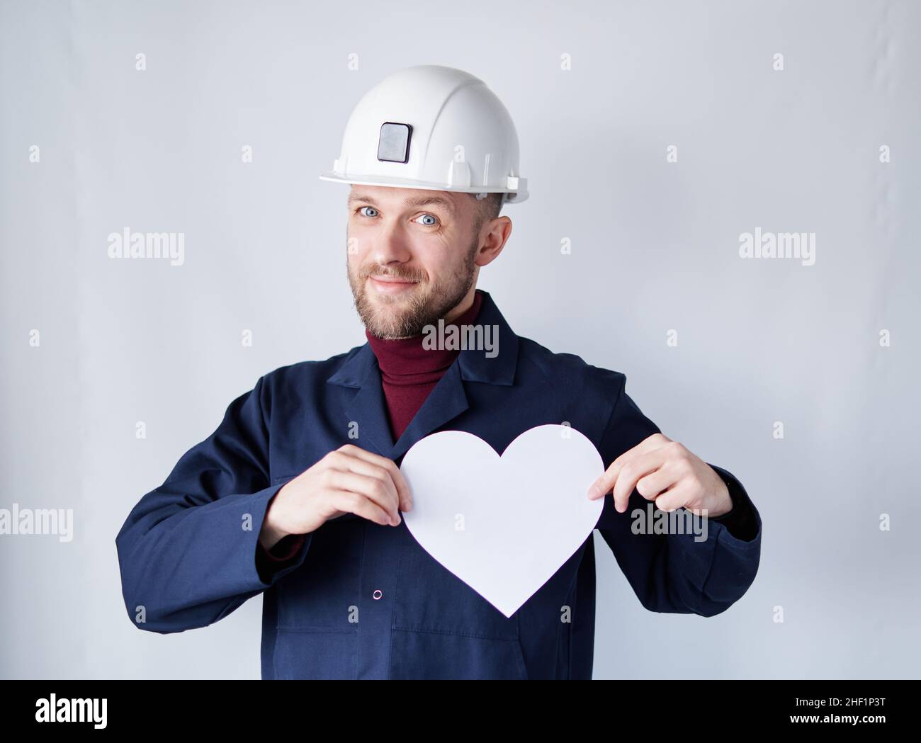 Saint-Valentin : technicien, entrepreneur, superviseur ou ingénieur de sexe masculin en casque de sécurité et uniforme bleu tenant en forme de coeur de papier blanc.Romance ou concept de relations.Image de haute qualité Banque D'Images