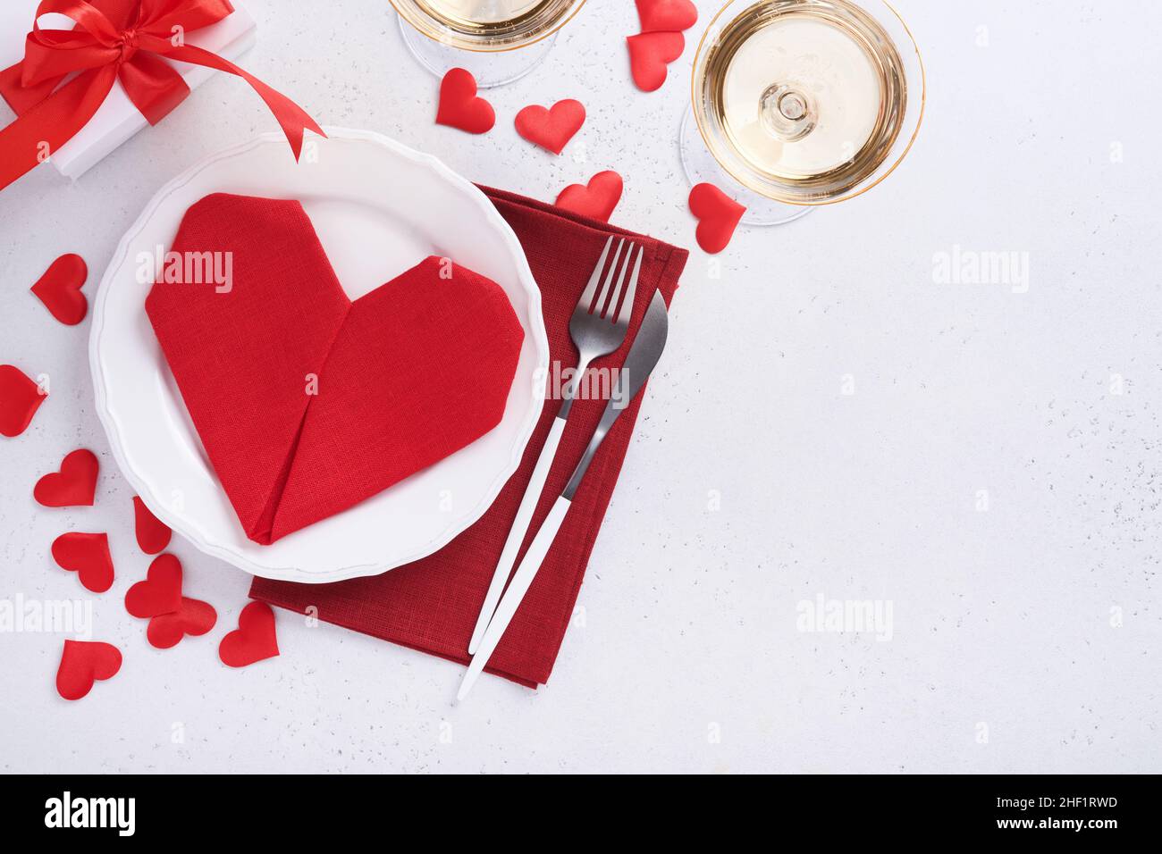 Table de jour de Valentinas couleur blanche avec argenterie blanche, serviette rouge pliée comme coeur, bougies, champagne, verres sur fond blanc pour greeti Banque D'Images
