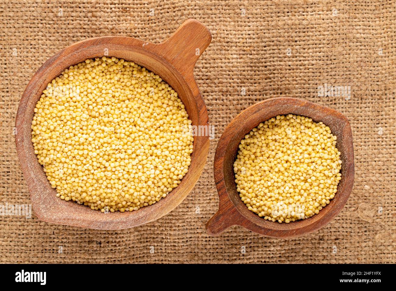 Gruaux de millet biologique brut dans deux tasses en bois sur le burlap, macro, vue de dessus. Banque D'Images