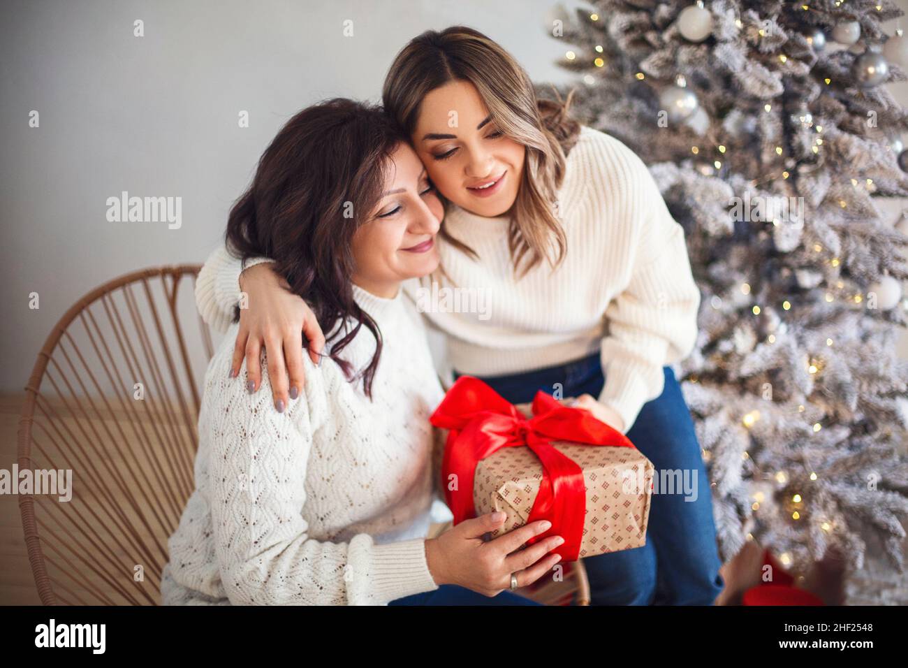 Bonne mère mature et fille adulte échangeant des cadeaux de Noël et embrassant tout en étant assis près de l'arbre de Noël à la maison.Jeune femme félicitant l'aîné Banque D'Images