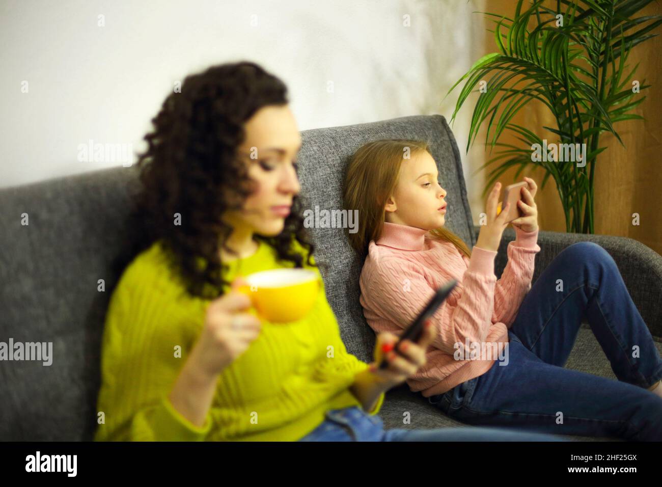 Une jeune mère et une petite fille focalisées sur les téléphones portables tout en étant assis sur un canapé à la maison, un accent sélectif sur la détente de l'enfant sur le canapé Banque D'Images