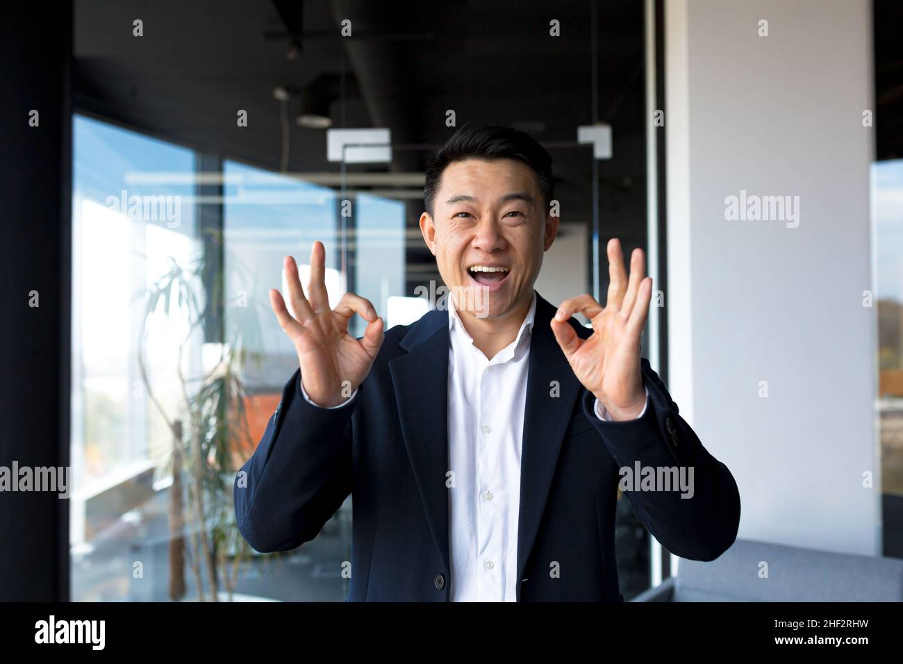 Portrait du propriétaire d'affaires réussi patron d'homme asiatique joyeux sourire et se réjouir dans le bureau moderne par grande fenêtre Banque D'Images