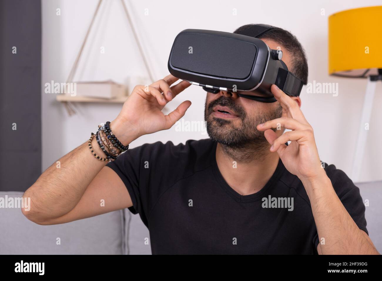 Jeune homme en VR lunettes casque à la maison en interaction avec la réalité virtuelle, gesturant. Future technologie, jeux vidéo éducatifs Banque D'Images