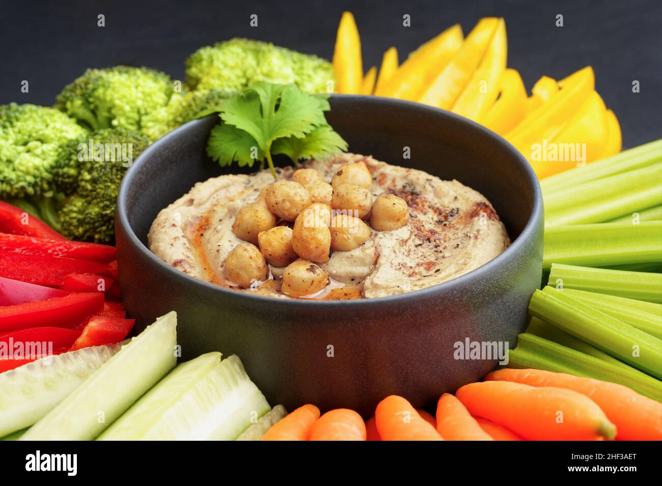 Houmous savoureux de pois chiches dans une assiette noire avec légumes frais et paprika fumé Banque D'Images