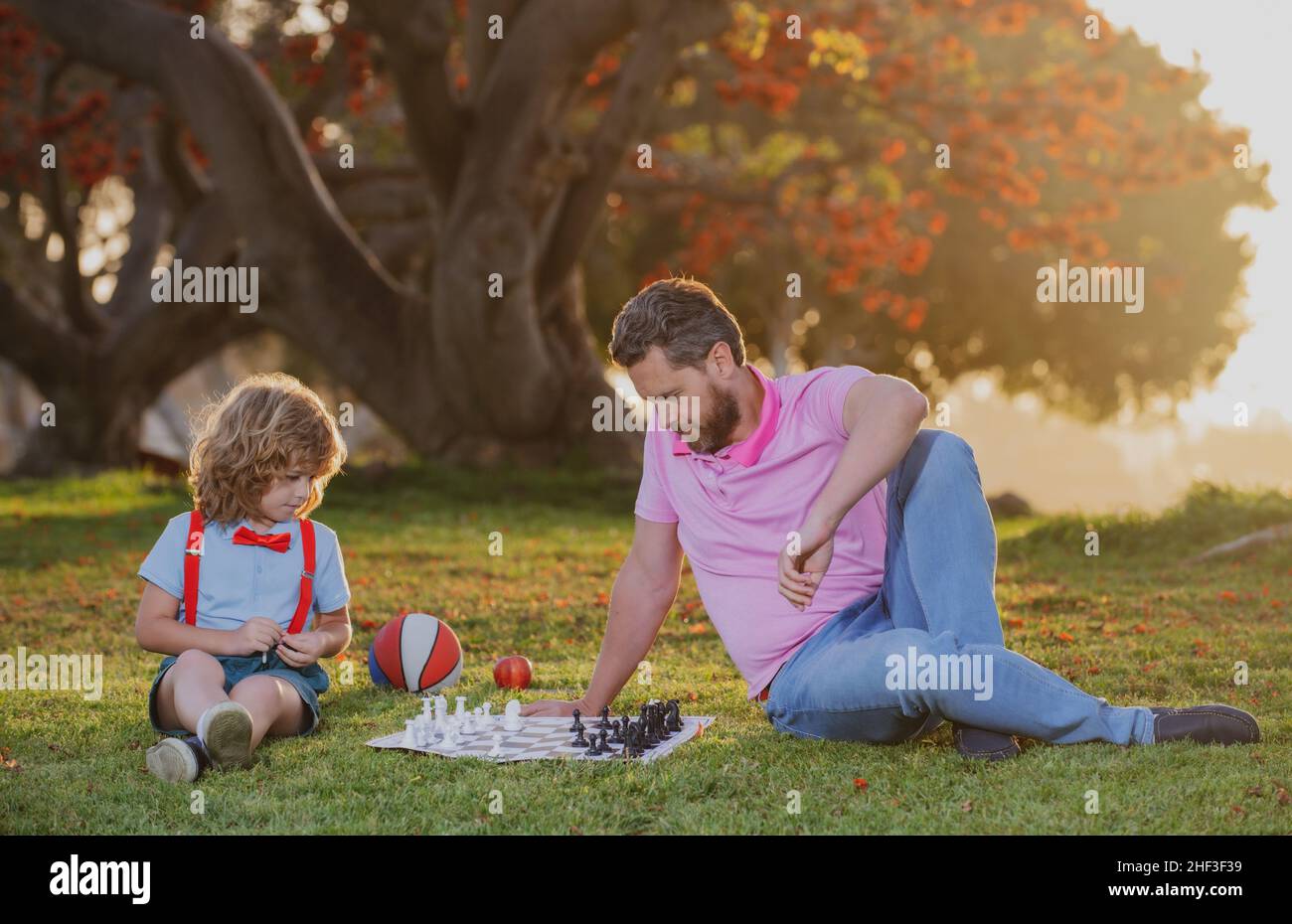 École d'échecs pour enfants.Père et fils jouant aux échecs allongé sur l'herbe au parc de pelouse.Fête des pères, famille d'amour, parentalité, concept d'enfance.Enfant concentré Banque D'Images