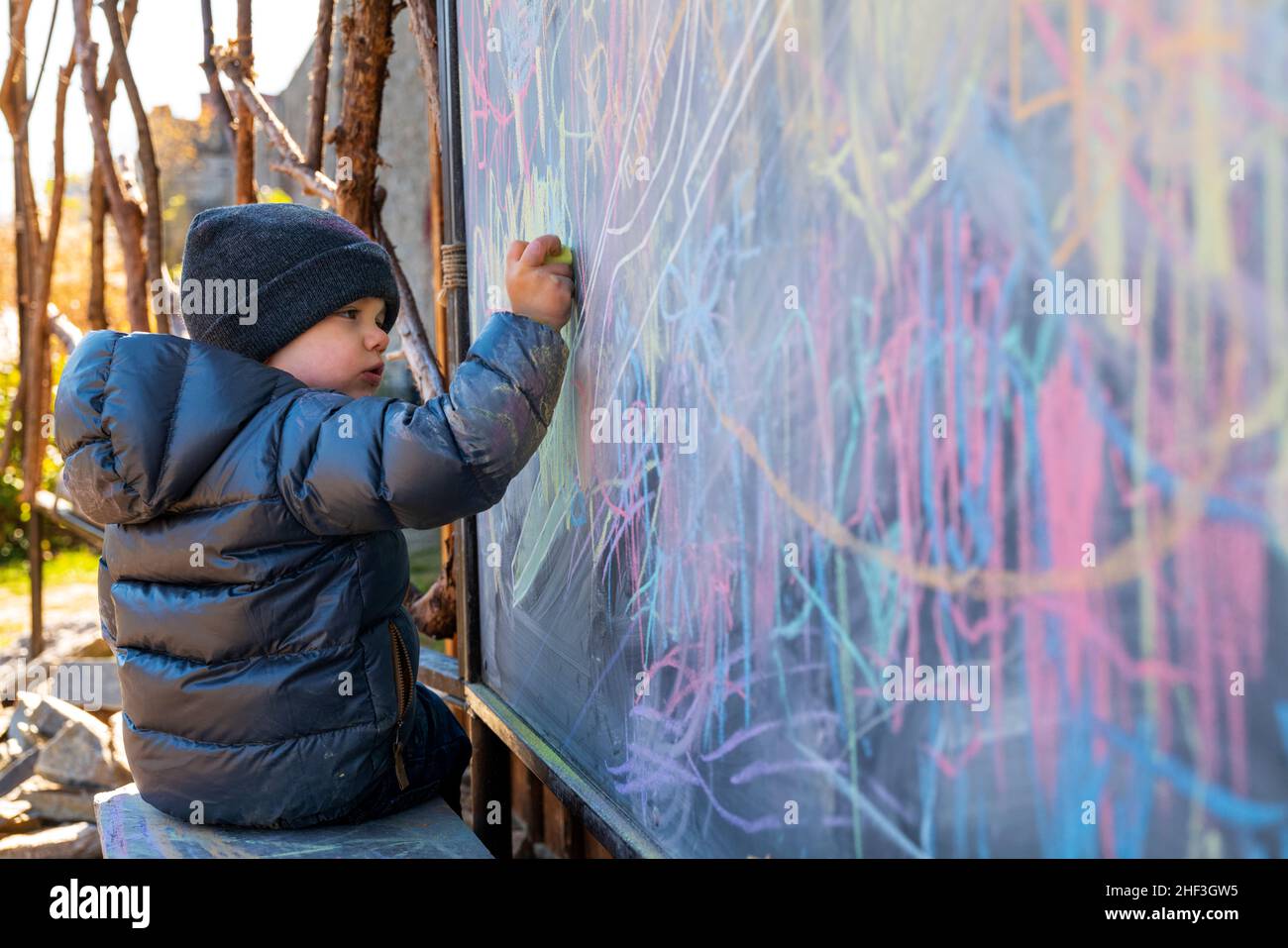 Un garçon de deux ans dessine avec de la craie colorée sur le tableau de craie du parc de la ville Banque D'Images