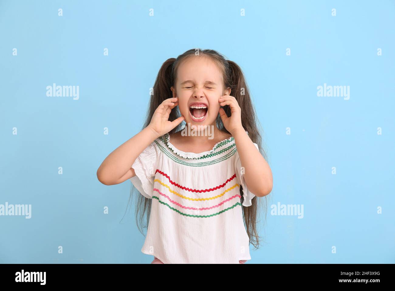 Portrait d'une petite fille en colère avec queue de cheval sur fond bleu Banque D'Images