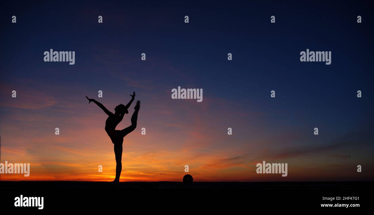 Danseuse dans la dance ne le divise dans l'air contre le coucher du soleil Banque D'Images