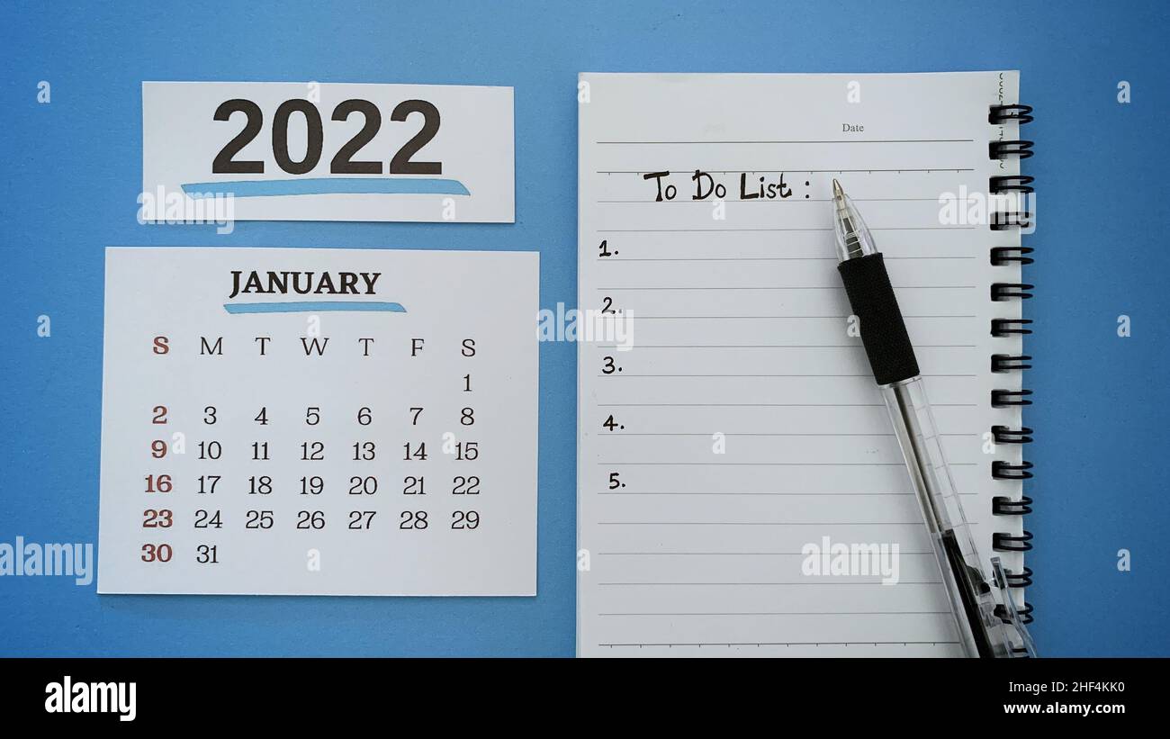 Liste des tâches texte écrit à la main sur un bloc-notes avec calendrier du mois de janvier 2022 et fond bleu. Banque D'Images