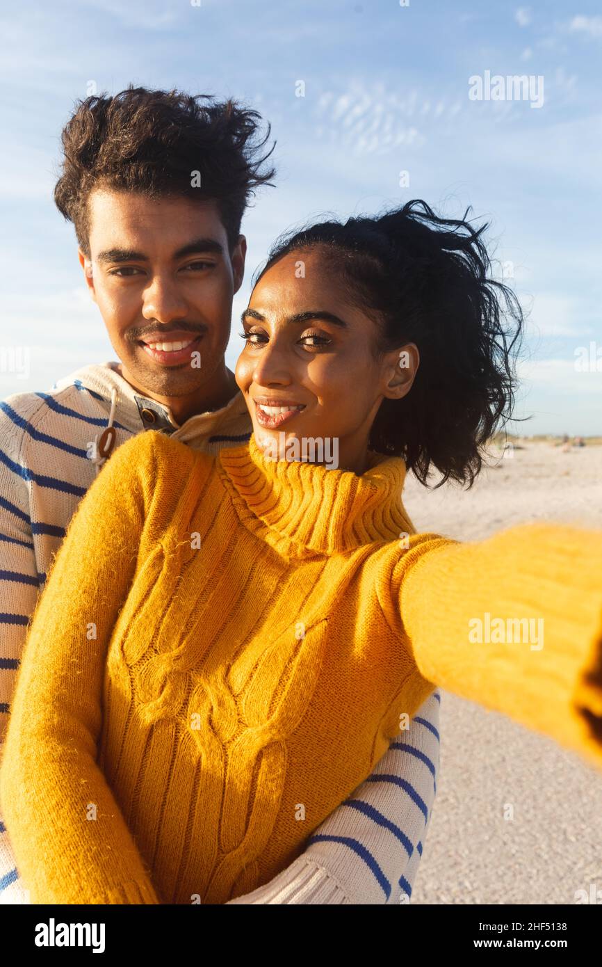Portrait de jeune souriant belle femme biraciale prenant selfie avec petit ami à la plage contre le ciel Banque D'Images