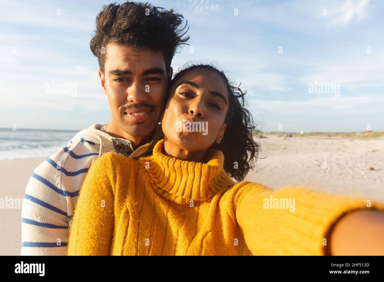 Portrait d'une jeune femme biraciale en train de pister tout en prenant selfie avec un petit ami à la plage le jour ensoleillé Banque D'Images
