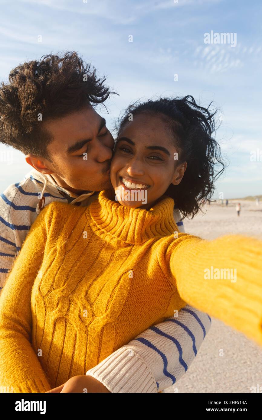 Portrait d'une femme biraciale souriante prenant le selfie d'un petit ami embrassant et embrassant sur la joue à la plage Banque D'Images