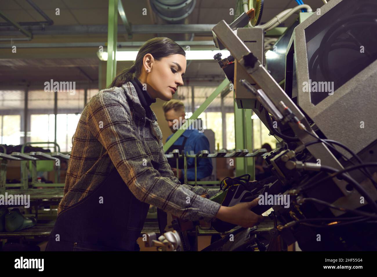 Femme utilisant une presse industrielle spéciale tout en faisant de nouvelles baskets à l'usine de chaussures Banque D'Images