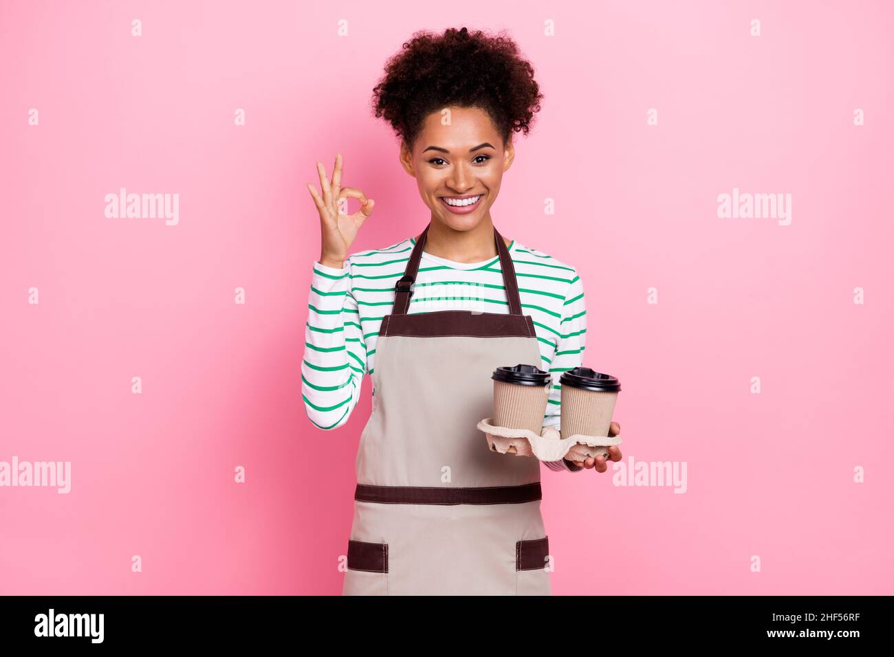 Photo de gai fiable fille tenir le café montrer symbole okey approuver la qualité usure tablier isolé couleur rose fond Banque D'Images