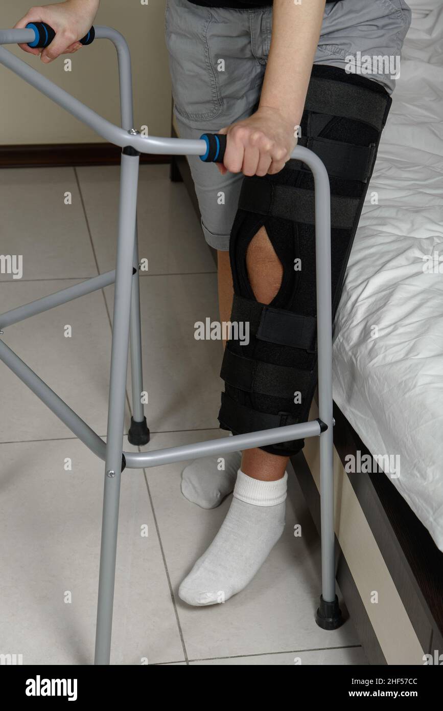 Femme portant un étrésillon de jambe après une intervention chirurgicale sur une fracture du genou essayant de marcher avec un marcheur.Réadaptation après une blessure.Gros plan Banque D'Images