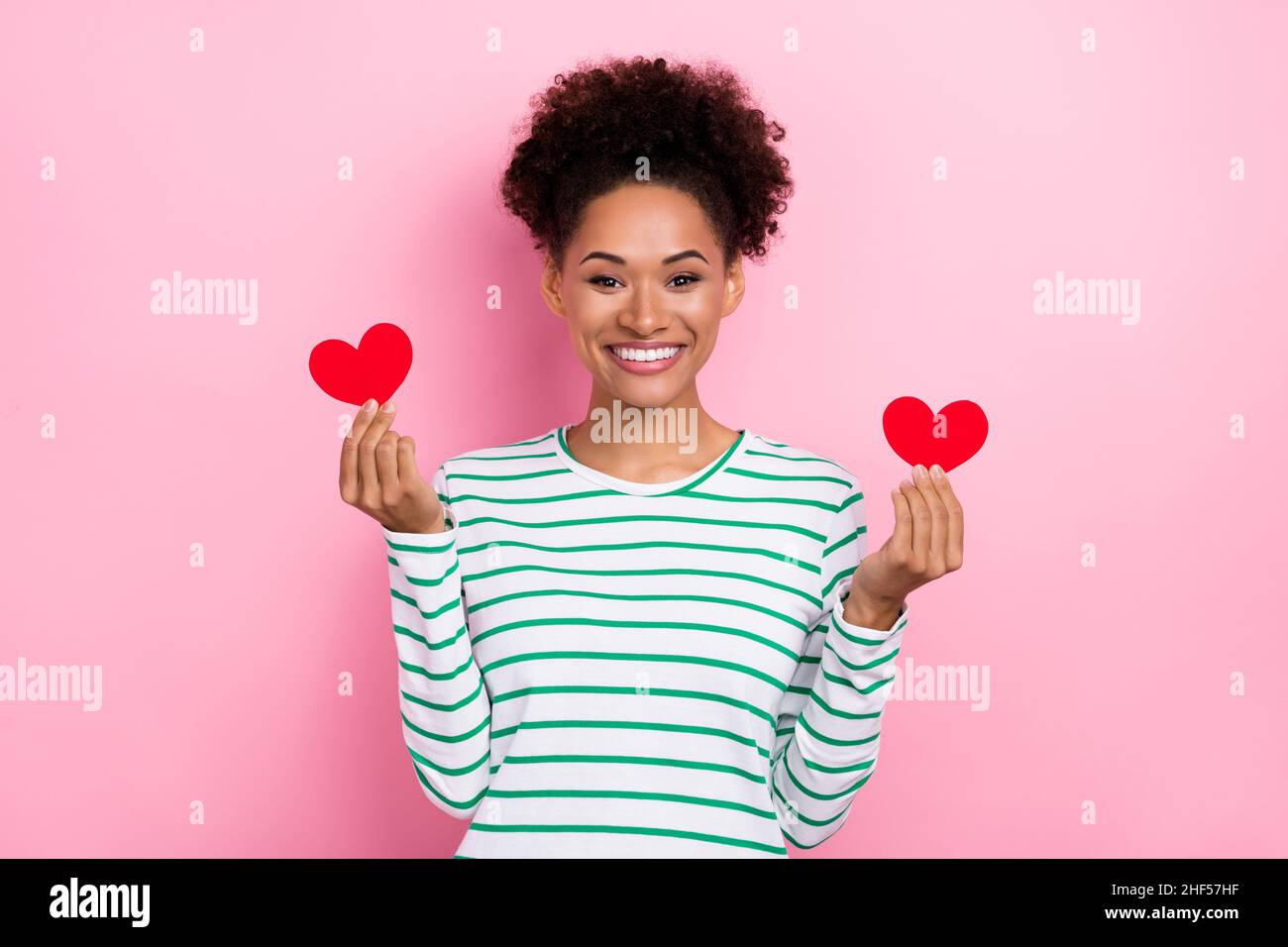 Photo de flirty bun coiffure jeune dame tenir les coeurs porter chemise blanche isolée sur fond de couleur rose Banque D'Images